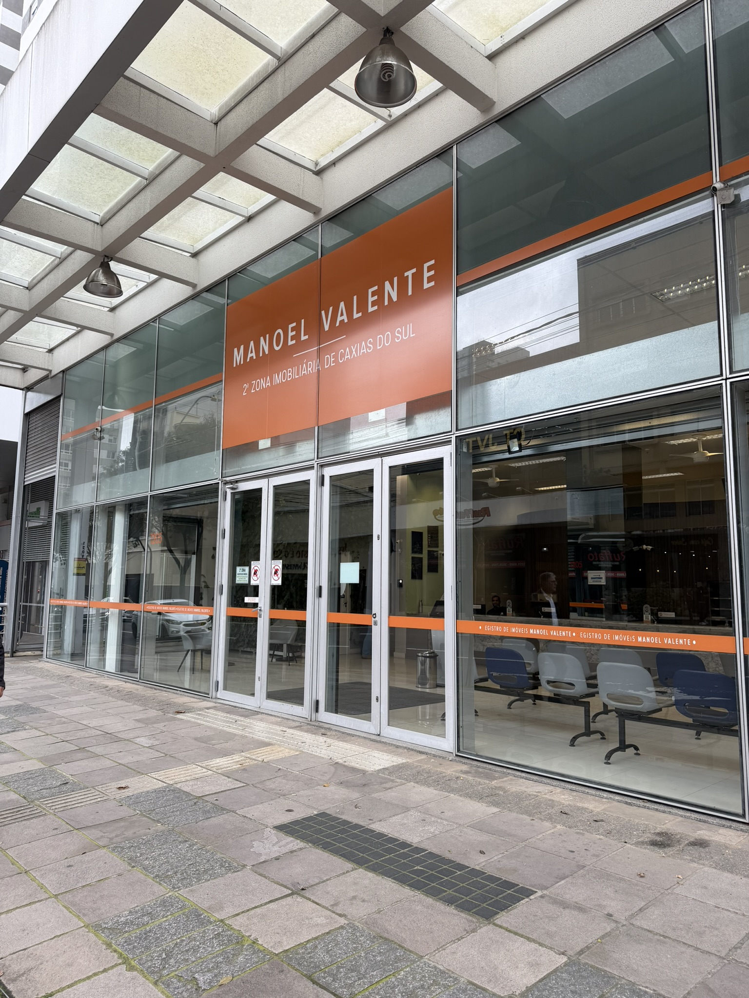 Fachada de vidro da sede, com a identificação "Manoel Valente — 2ª Zona Imobiliária de Caxias do Sul" e o número do endereço na porta de entrada.